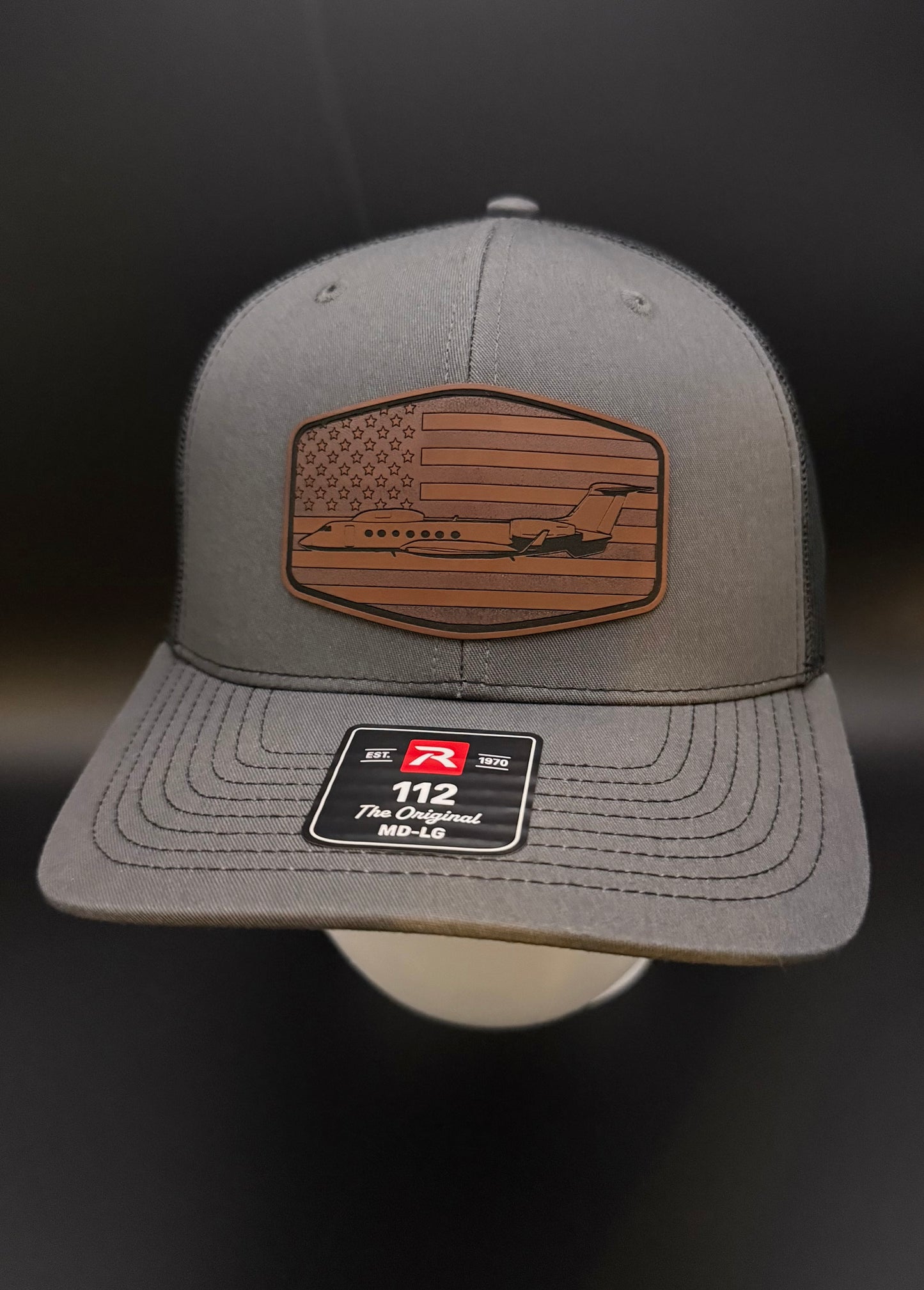 Gray cap with American flag patch and logo on a dark background
